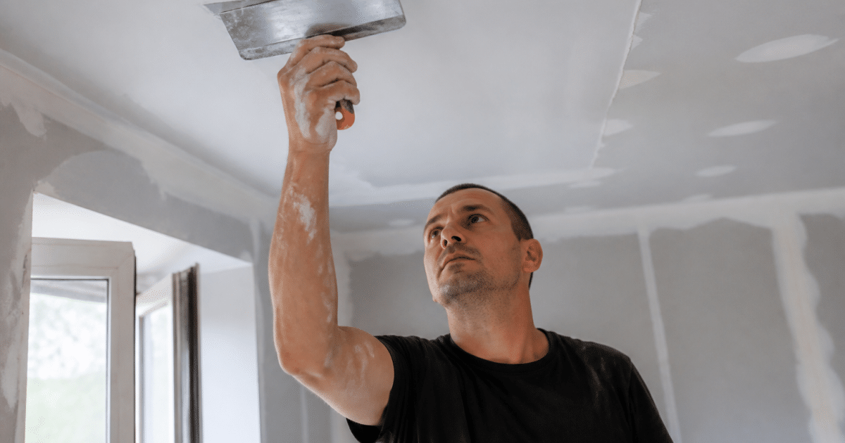 Ouvrier appliquant placo sur plafond avec spatule large