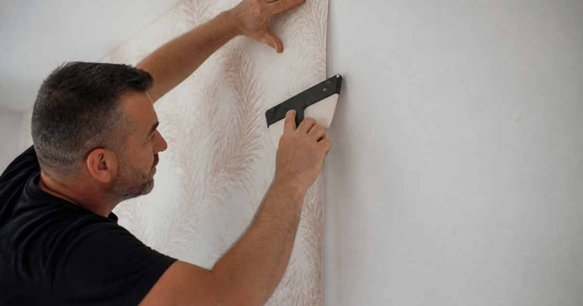 Mains appliquant papier peint sur mur blanc avec raclette